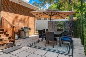 Eine Terrasse im Freien mit Grill, Esstisch, Stühlen und einem Zierzaun.