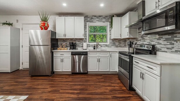A modern kitchen with white cabinets, stainless steel appliances, and a wooden floor. - Butterfly Bungalow is a 4BR/2BA home with outdoor terrace and grill (Columbus)