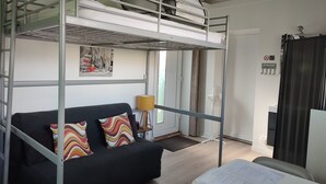 A bunk bed room with a black sofa and colorful pillows, a lamp, and a door with a 'So welcome' sign. - Fully-equipped 1 room furnished studio without partitions (Chavagnes-en-Paillers)