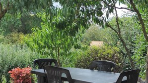 An outdoor dining area with a table and chairs, surrounded by trees and greenery. - Fully-equipped 1 room furnished studio without partitions (Chavagnes-en-Paillers)