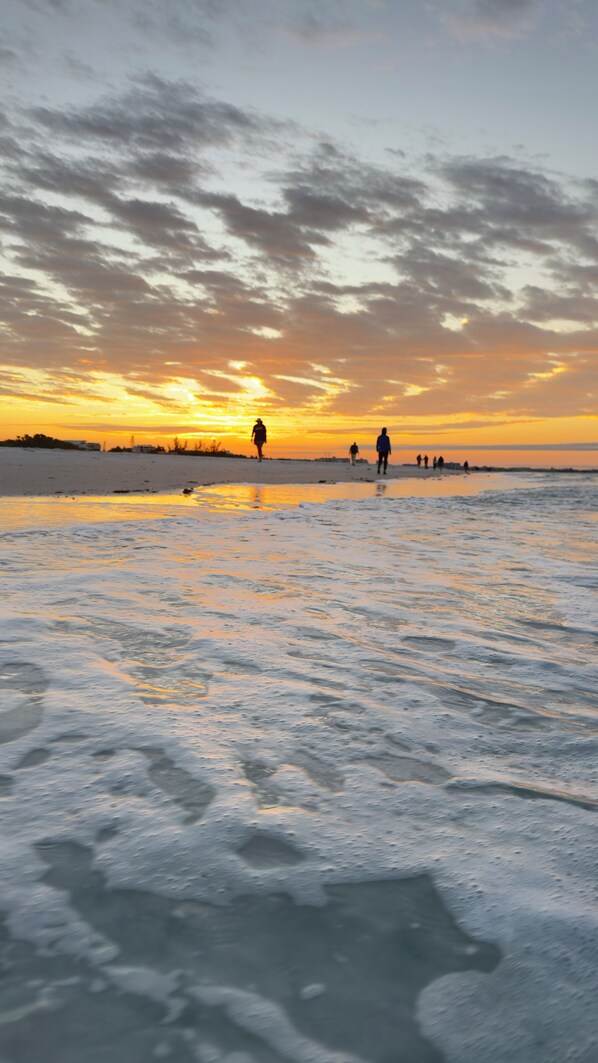 A beach scene with people walking along the shore during sunset.