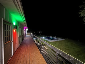 A wooden deck with a pool, a fenced area, and a building with illuminated windows.