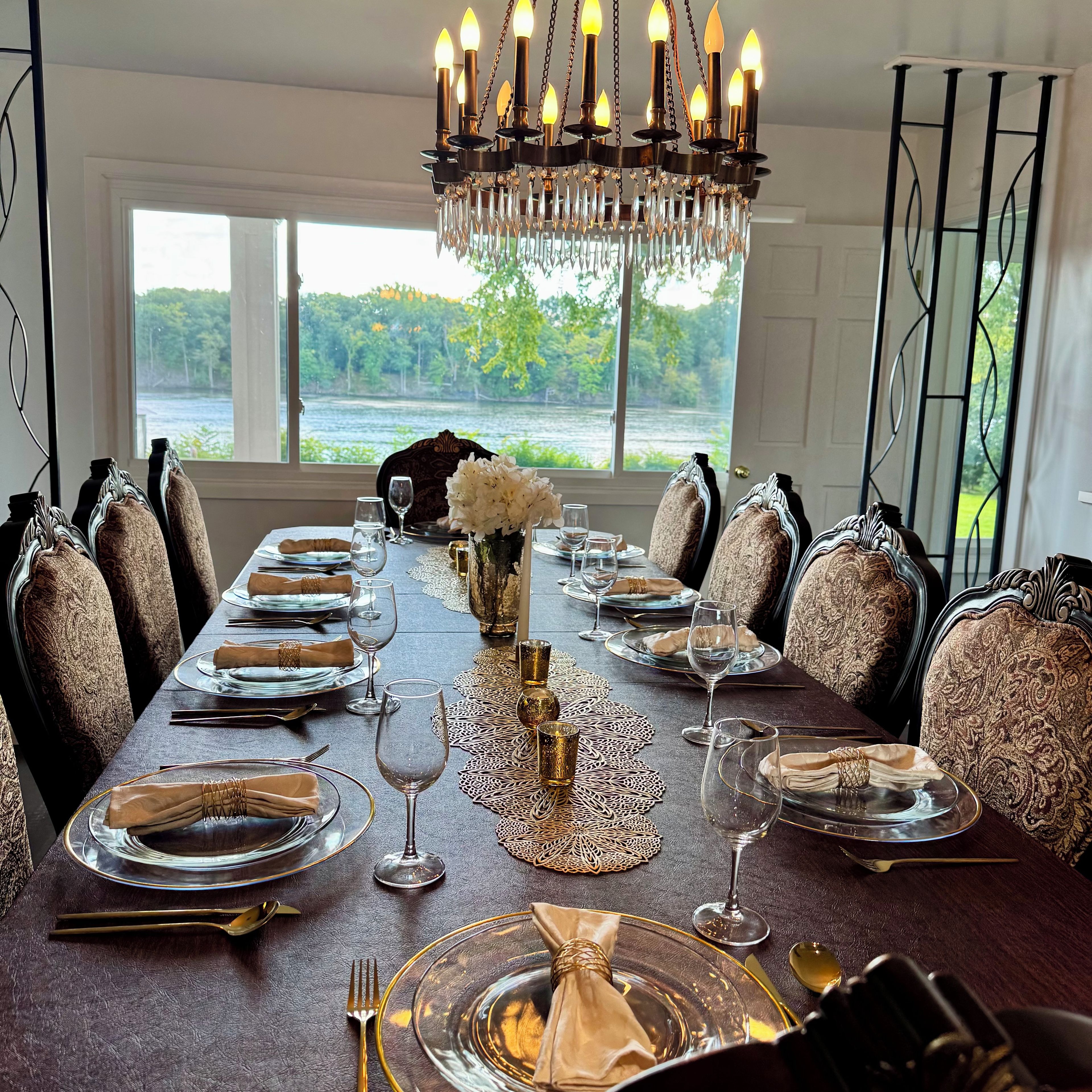 A formal dining room with a long table set for a meal, elegant chairs, and a chandelier.