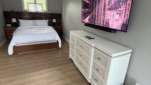 Ein Schlafzimmer mit einem Bett, einer weißen Kommode, einem Flachbildfernseher und einem Fenster.