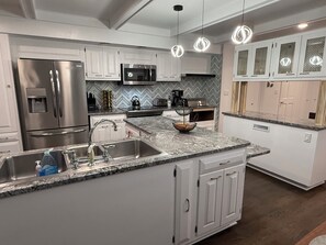 A modern kitchen with white cabinetry, stainless steel appliances, a granite countertop, and pendant lighting.