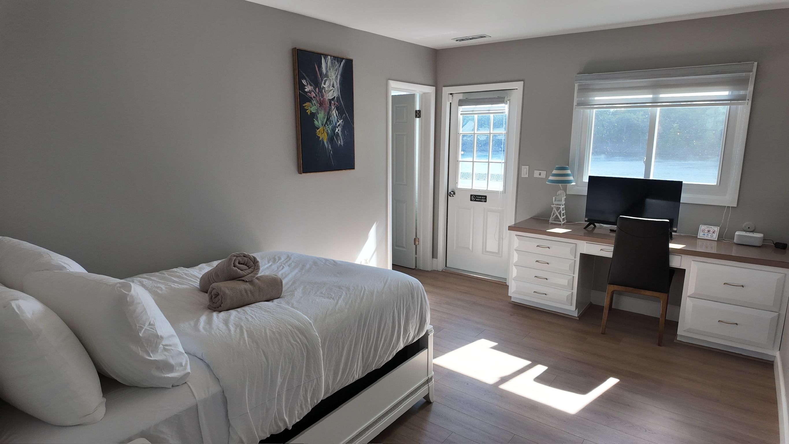 A bedroom with a bed, a desk, and a chair. There is a door leading to another room.