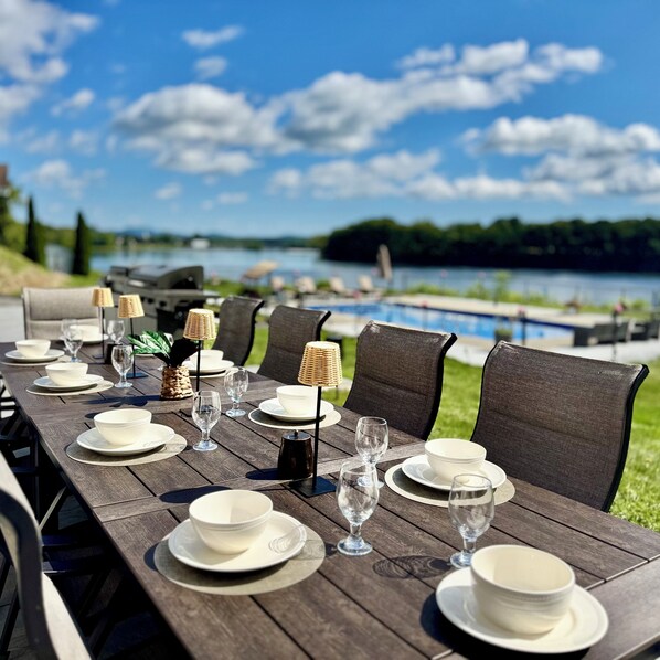 A dining table set with plates, glasses, and a lamp, overlooking a body of water.