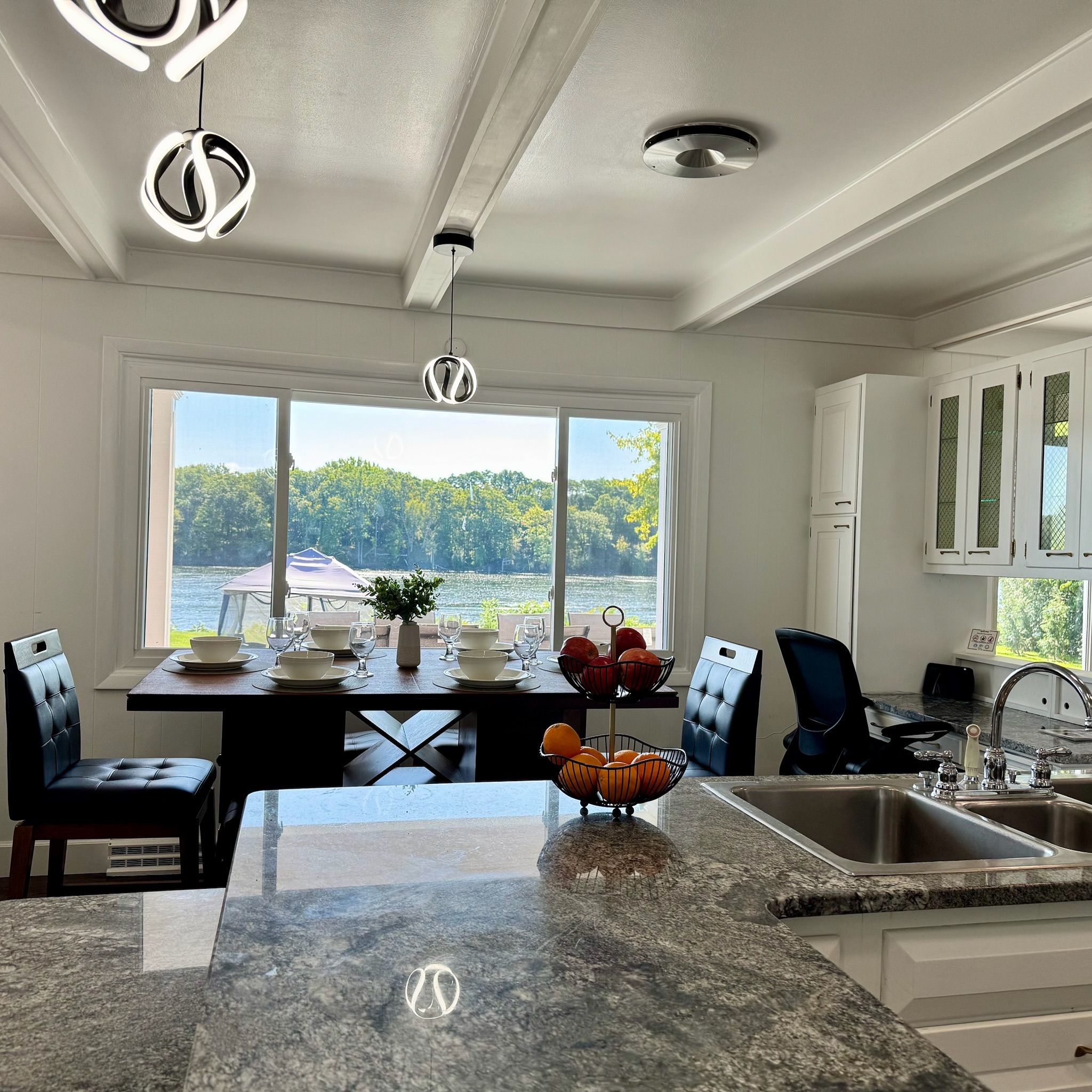 A modern kitchen with a large island, a dining area with a view of a lake, and a view of the outdoors.