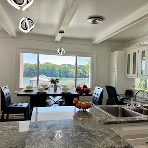 A modern kitchen with a large island, a dining area with a view of a lake, and a view of the outdoors.