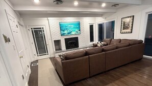 Ein modernes Wohnzimmer mit einem braunen Ecksofa, einem Kamin und einem großen Fernseher, der an einer weißen Ziegelwand angebracht ist.