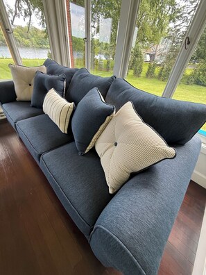 A dark blue sofa with striped and solid pillows, positioned near a large window with a view of a lake and greenery.