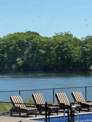 A pool area with lounge chairs and a view of a lake surrounded by trees.