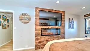A bedroom with a large bed, a wooden accent wall, a TV, and a fireplace. - Spacious 2 Bedroom 2 Bath Lake View Condo (Laconia)