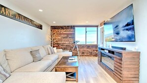 A modern living room with a sofa, coffee table, and a large TV on a wooden stand. - Spacious 2 Bedroom 2 Bath Lake View Condo (Laconia)