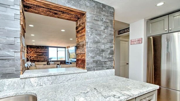 A modern kitchen with a stone backsplash, a stainless steel refrigerator, and a sign indicating a 'Lake House' room. - Spacious 2 Bedroom 2 Bath Lake View Condo (Laconia)