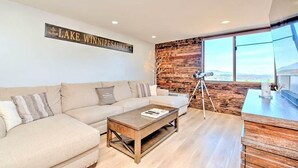 Una sala de estar moderna con un gran ventanal, una pared de acento de madera, un sofá, una mesa de centro y un telescopio.