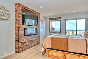 A bedroom with a rustic wooden wall, a bed with a beige cover, and a large window offering a view of the outdoors. - Adorable Cedar Lodge Room w/ Lake Views! (Laconia)