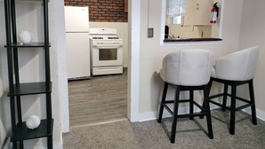A kitchen with a white refrigerator, stove, and oven, a black shelf with decorative items, and two white chairs. - Charming 3-bedroom house in peaceful Binghamton, close to downtown, with ACs (Binghamton)