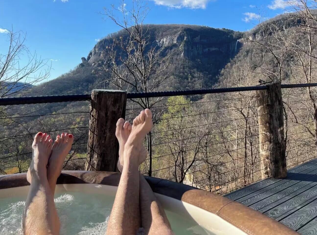 A person relaxing in a hot tub with a mountainous landscape in the background.