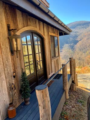 Eine Holzhütte mit einer großen Haustür, einem kleinen Fenster und einer Veranda mit Geländer.