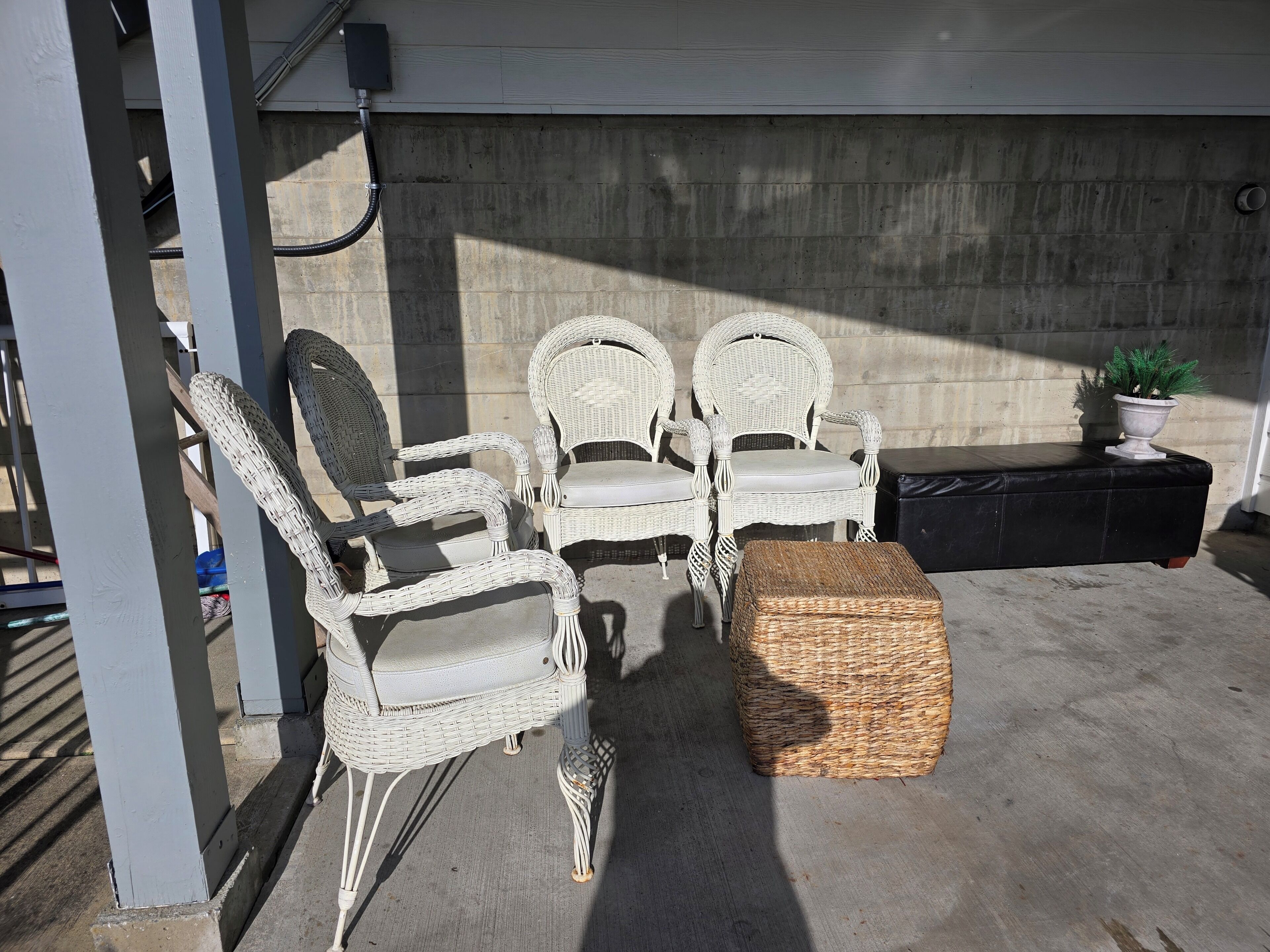 A patio with wicker chairs, a woven ottoman, and a potted plant.