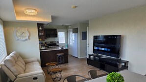 A modern living room with a sofa, a dining table, a TV, and a kitchen area with a bar. - Mountain House: An apartment with a gorgeous ocean view on Triangle Mountain. (Victoria)