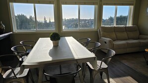 A dining area with a table, chairs, a potted plant, and a sofa. - Mountain House: An apartment with a gorgeous ocean view on Triangle Mountain. (Victoria)