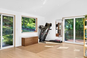 A modern room with a treadmill, large windows, and a view of greenery. - Dartmouth Graduation—Luxury MCM Home in Hanover (Hanover)