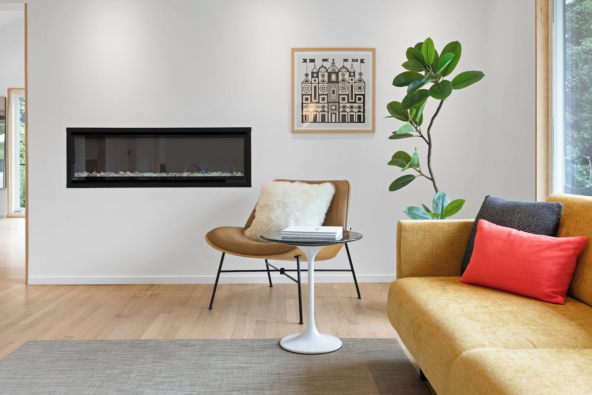 A modern living room with a fireplace, a sofa, a chair, and a plant.