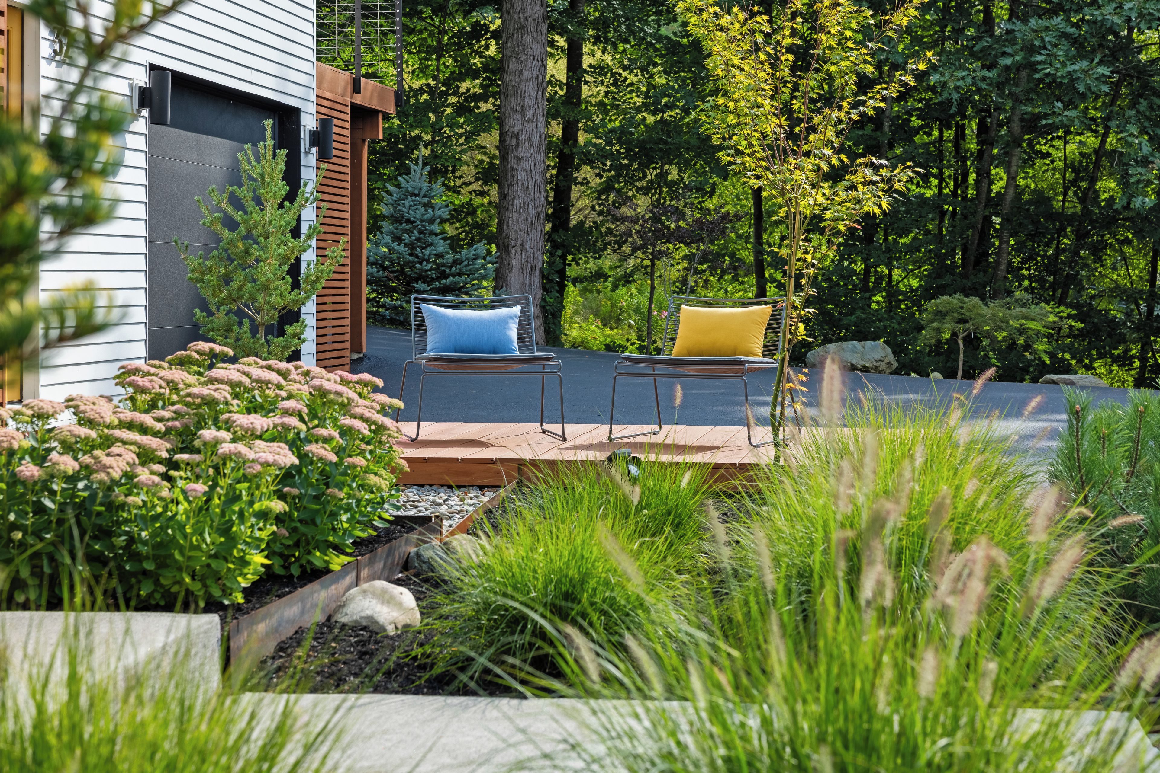 An outdoor seating area with two chairs and a table, surrounded by greenery and a wooden deck.