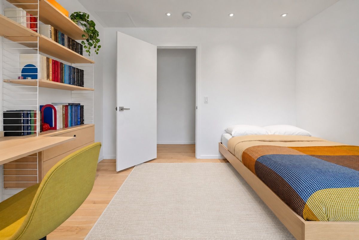 A bedroom with a bed, a desk with a chair, a bookshelf, and a door leading to another room.