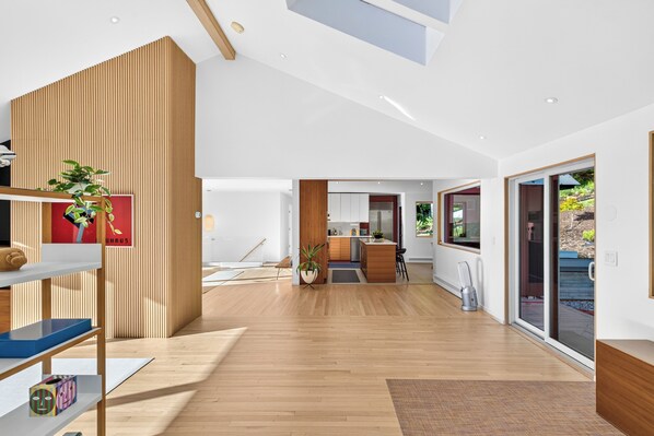 A spacious interior with a wooden floor, a kitchen area, and a large sliding glass door leading to an outdoor area. - Dartmouth Graduation—Luxury MCM Home in Hanover (Hanover)