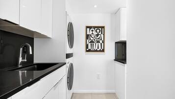 A compact kitchen with a black countertop, stainless steel faucet, and a washing machine.