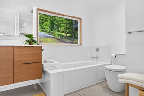 A modern bathroom with a bathtub, toilet, and a large window with a forest view. - Dartmouth Graduation—Luxury MCM Home in Hanover (Hanover)