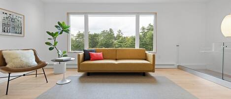 A modern living room with a sofa, a chair, a plant, and a large window.