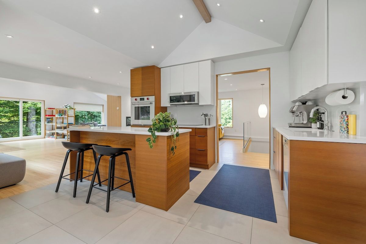 A modern kitchen with a central island, bar stools, and a view of the outdoors.