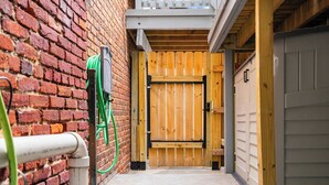 A narrow alleyway with a wooden gate, a brick wall, and a garage door. - Cozy in Canton - Private Driveway - Pet Friendly (Baltimore)