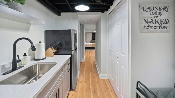 A modern kitchen with a stainless steel sink, black faucet, and a refrigerator. There is a sign on the wall that reads "Laundry today or naked tomorrow." - Cozy in Canton - Private Driveway - Pet Friendly (Baltimore)