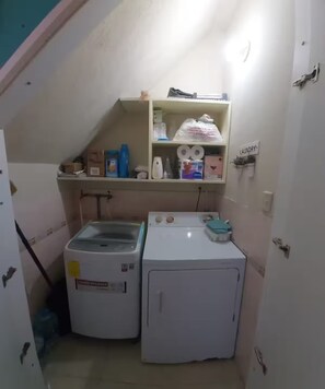 A laundry room with a washing machine, dryer, and shelves containing cleaning supplies. - Confortable Departament Cabin
Entire guest suite in Olon, Ecuador (Olon-Santa Elena)