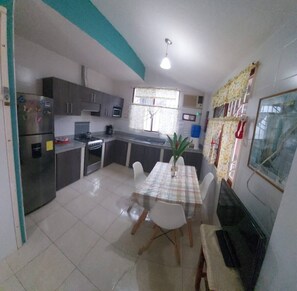 Una cucina compatta con zona pranzo, frigorifero, fornelli e finestra con tende.