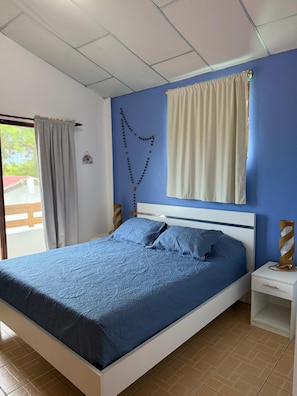 A bedroom with a bed, a nightstand, a window with curtains, a wall decoration, and a view of the outdoors. - Confortable Departament Cabin
Entire guest suite in Olon, Ecuador (Olon-Santa Elena)