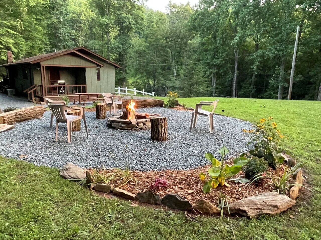 Un espace extérieur rustique aménagé avec des sièges, un foyer entouré d’un cercle de gravier et une terrasse en bois avec des chaises.