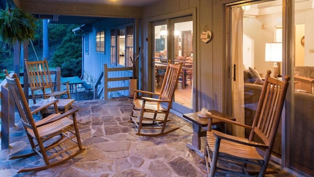 Un patio con pavimento in pietra, poltrone a dondolo in legno e una porta in vetro che dà su un ambiente interno.