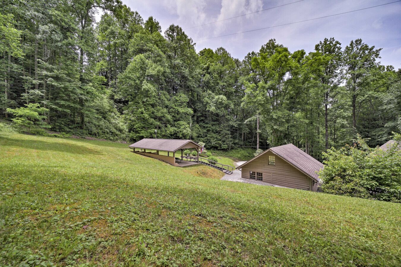 A cabin with a porch and a covered picnic area, surrounded by dense forest.