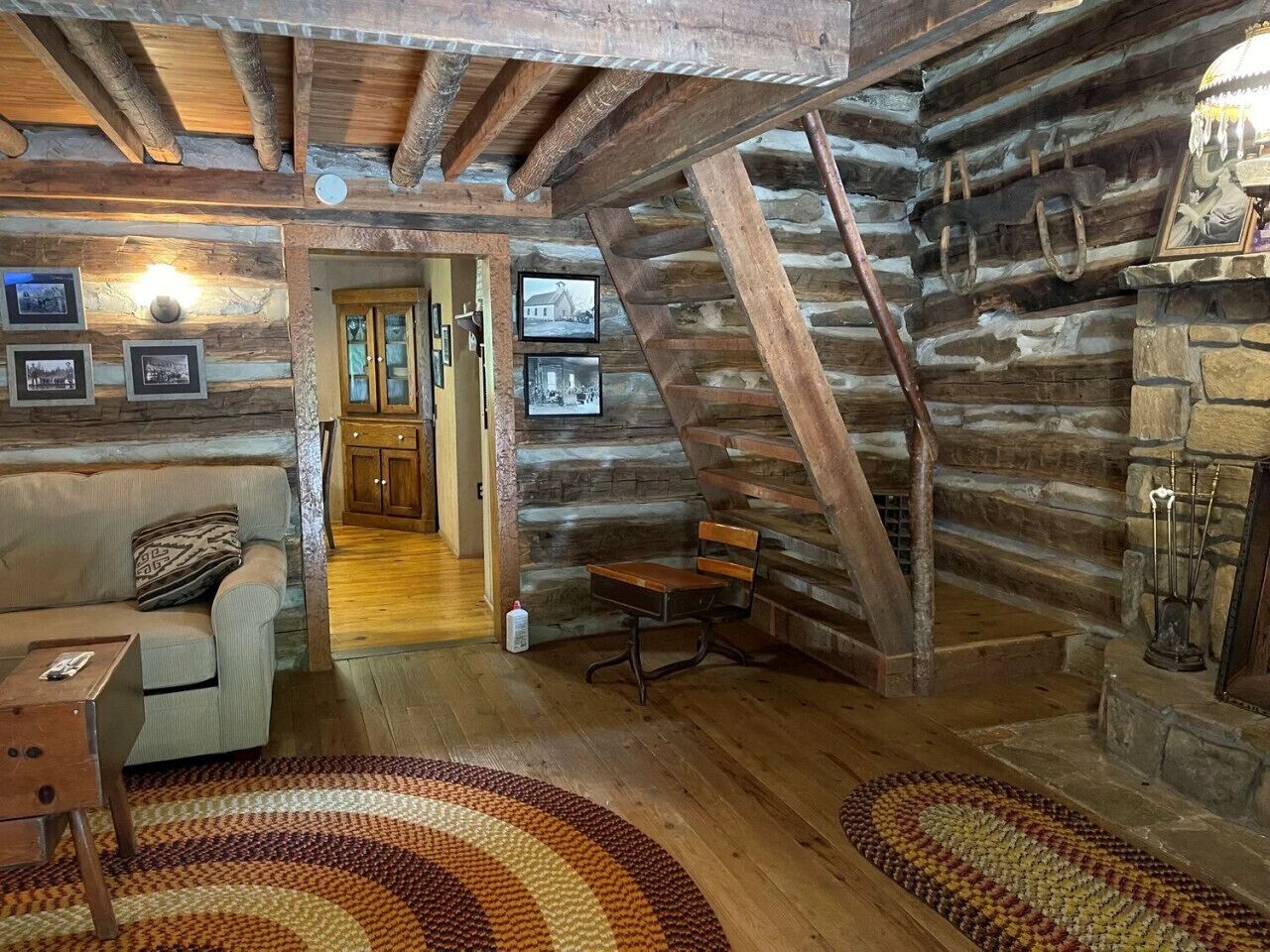 A rustic log cabin interior with a wooden staircase, a sofa, a small table, and a fireplace.