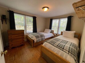 Une chambre à coucher avec deux lits en bois, une commode en bois et une fenêtre avec des rideaux.