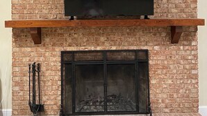 A brick fireplace with a flat-screen TV mounted above it. - Masters 2027 Secluded Charming House in the Pines (Harlem)