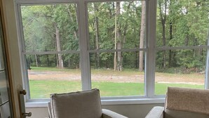 A room with two beige armchairs, a patterned rug, and a large window offering a view of a wooded area. - Masters 2027 Secluded Charming House in the Pines (Harlem)
