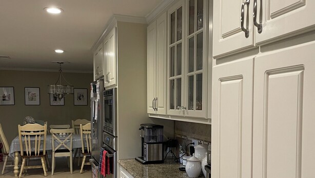A kitchen with white cabinets, a granite countertop, and a dining area with wooden chairs and a table. - Masters 2027 Secluded Charming House in the Pines (Harlem)