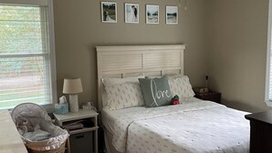 A bedroom with a bed, a nightstand, a lamp, a crib, and a ceiling fan. - Masters 2027 Secluded Charming House in the Pines (Harlem)